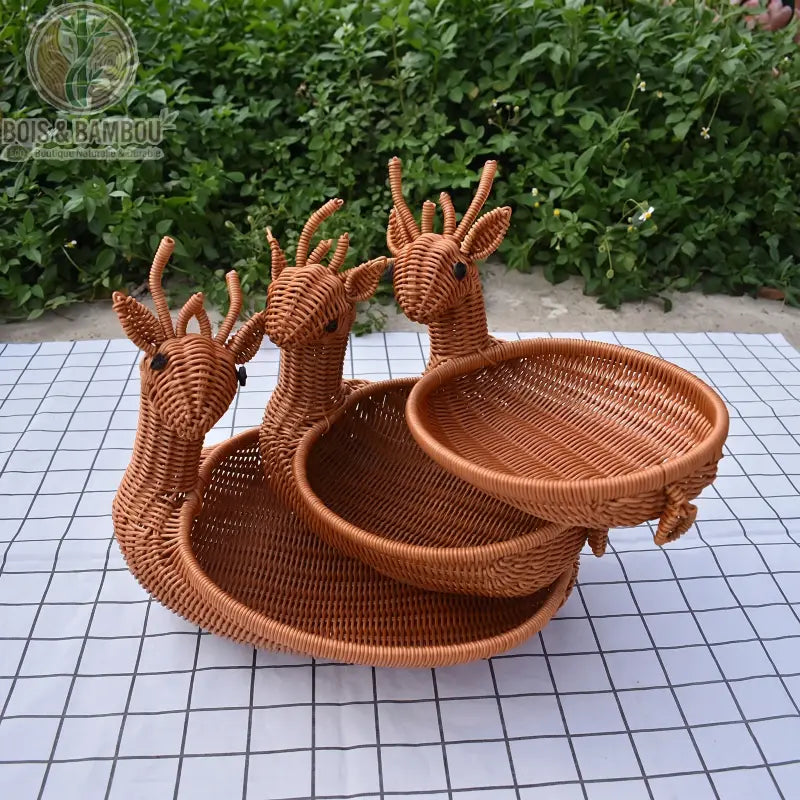 Corbeille à fruits en rotin tressé. Trois paniers en rotin tressé en forme de cerfs de tailles différentes, disposés sur une nappe à carreaux en extérieur. Design original et ludique.