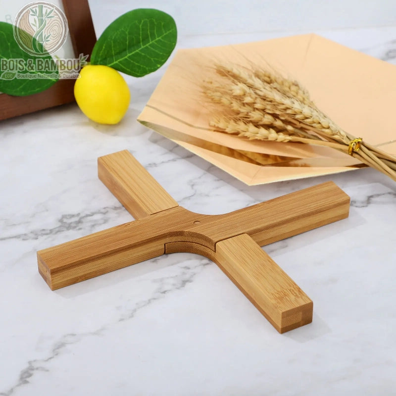Dessous de Plat Pliable et Extensible. Un dessous de plat en bambou en forme de X sur une table en marbre, avec un citron et des épis de blé en arrière-plan.