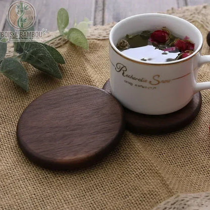 Dessous de Verre en Bois Massif. Deux dessous de verre circulaires en bois sombre, l'un supportant une tasse de thé blanc avec des boutons de rose sur un tissu en toile de jute.