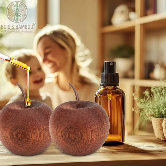 Diffuseur d'arômes en bois naturel, deux diffuseurs passifs sculptés en forme de pommes en bois sombre avec une tige fine, montrés sur une table à côté d'un flacon pulvérisateur, tandis qu'une pipette verse une goutte d'huile dorée sur l'un d'eux dans une ambiance familiale chaleureuse.