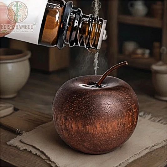 Diffuseur d'huiles essentielles en bois minimaliste, un objet décoratif sculpté en forme de pomme dans un bois sombre et texturé, présenté avec une main versant une goutte d'huile essentielle sur le sommet pour une diffusion naturelle.