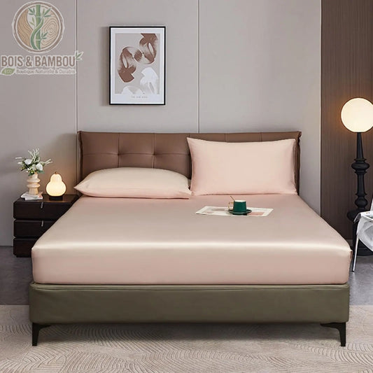 Drap-Housse en Bambou Rose 90x200 cm. Un lit élégant habillé d'un drap-housse et de deux oreillers rose poudré à l'aspect satiné, dans une chambre moderne et chaleureuse.