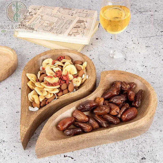 Duo de Plateaux Cœur Modulable. Deux plateaux artisanaux en manguier imbriqués formant un cœur, l'un rempli de fruits secs, l'autre de dattes, avec un verre de vin.