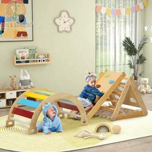Ensemble d'Escalade 7-en-1 Montessori. Un bébé et un enfant jouent sur une structure en bois avec arche colorée, triangle de Pikler et rampe d'escalade sur un tapis dans une chambre.