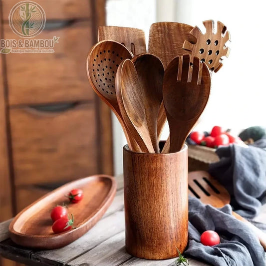 Ensemble d'ustensiles de cuisine en bois de teck massif. Une variété d'ustensiles (spatules, louches, fourchettes) rangés dans un pot cylindrique en bois sur une table rustique.