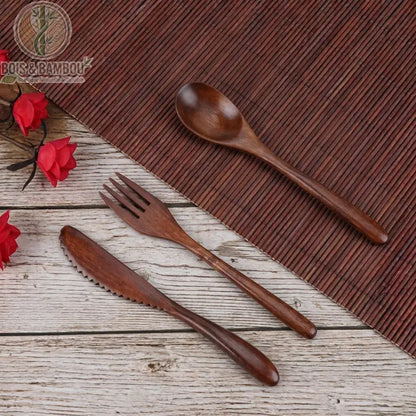 Ensemble de vaisselle en bois réutilisable. Un set comprenant une cuillère, une fourchette et un couteau dentelé en bois sombre, disposés sur une table rustique avec un set en bambou.