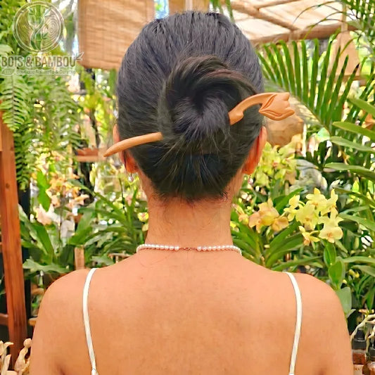 Épingle à Cheveux en Bois de Pêcher sculptée en forme de tulipe, maintenant le chignon d'une femme de dos dans un décor de jardin tropical luxuriant.