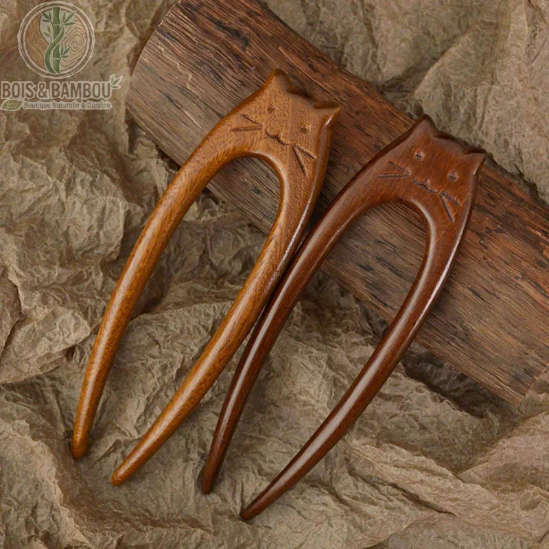 épingle à cheveux en bois chat sculptée deux dents posées sur fond papier kraft bois foncé caramel