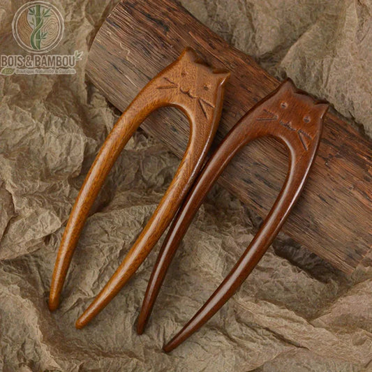 épingle à cheveux en bois chat sculptée deux dents posées sur fond papier kraft bois foncé caramel