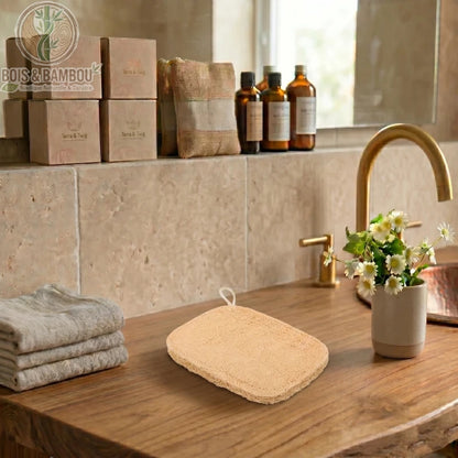 Éponges exfoliantes en luffa et bambou. Deux types d'éponges naturelles sur un meuble en bois, avec serviettes et décor de salle de bain zen. Idéal pour un gommage du corps écologique.