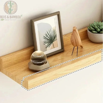 Etagere en bois massif flottante descriptif. Zoom sur une étagère en bois massif montrant son rebord de sécurité intégré, décorée d'un cadre photo, d'un oiseau sculpté et d'une petite plante.