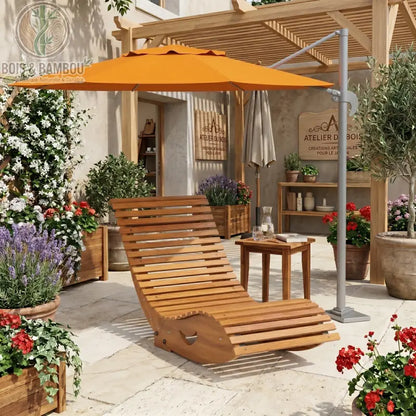 Fauteuil à Bascule Ergonomique. Un bain de soleil incurvé en lattes de bois clair placé sous un grand parasol orange déporté, sur une terrasse fleurie 