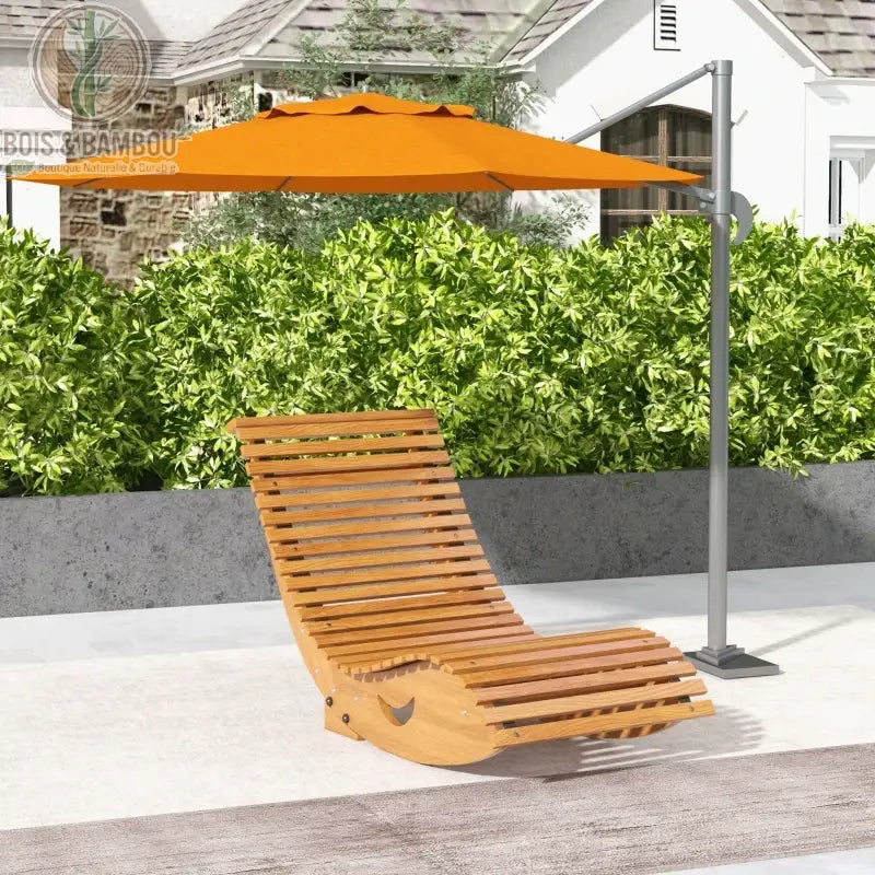Fauteuil à Bascule Ergonomique. Un bain de soleil incurvé en lattes de bois clair placé sous un grand parasol orange déporté, devant une haie verdoyante et une maison blanche.