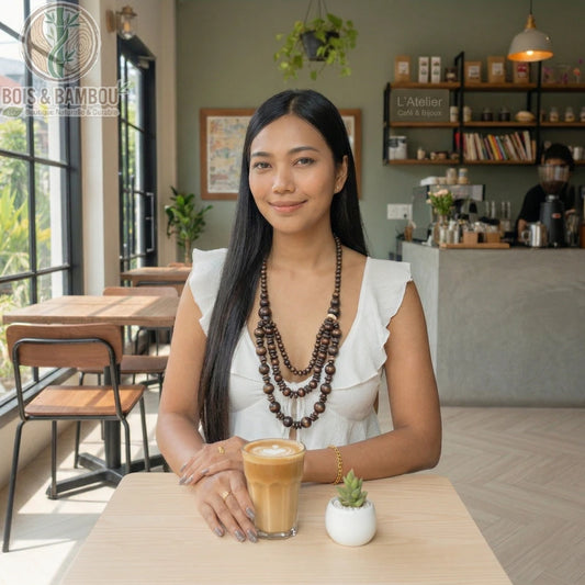 Long collier en perles de bois à plusieurs rangs porté par une femme dans un café moderne avec un latte sur la table.