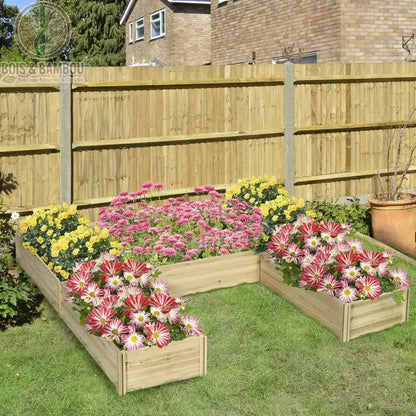 Grand Potager Modulable en Bois. Un grand bac de culture en bois clair en forme de U, généreusement fleuri de dahlias roses, jaunes et bicolores sur une pelouse devant une clôture.