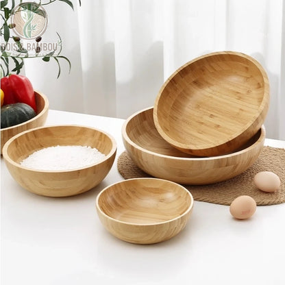 Grand bol en bambou naturel. Plusieurs bols ronds en bambou clair de tailles variées disposés sur une table blanche avec de la farine, des œufs et des légumes. Vaisselle écologique.