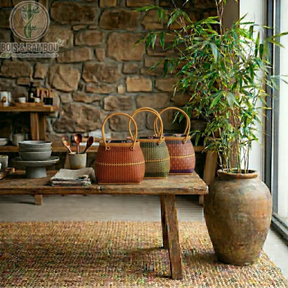 Grand fourre tout Nomade en bambou 5. Trois paniers artisanaux aux teintes terreuses et tressages variés, disposés sur un établi ancien dans un décor serein mêlant pierre brute et bambou naturel.