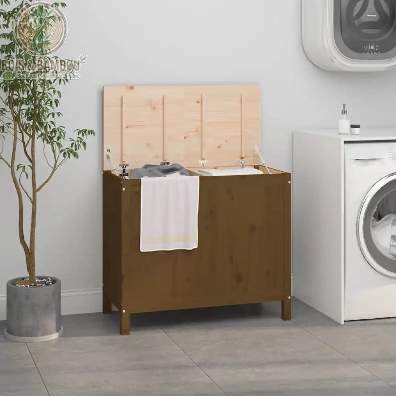 Grand panier a linge en bois de pin massif double marron. Coffre à linge double en bois marron avec couvercle ouvert révélant deux bacs distincts, situé dans une buanderie avec machine à laver.