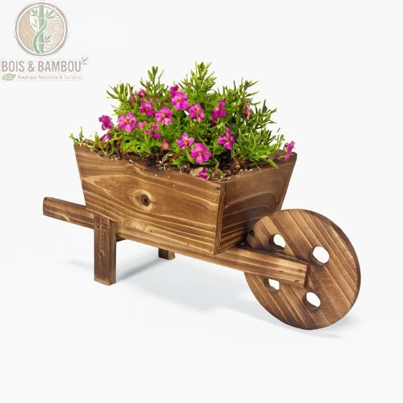 Jardinière Brouette en Bois. Une petite brouette décorative en bois brun rustique remplie de fleurs roses et de verdure, isolée sur un fond blanc épuré.