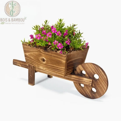 Jardinière Brouette en Bois. Une petite brouette décorative en bois brun rustique remplie de fleurs roses et de verdure, isolée sur un fond blanc épuré.