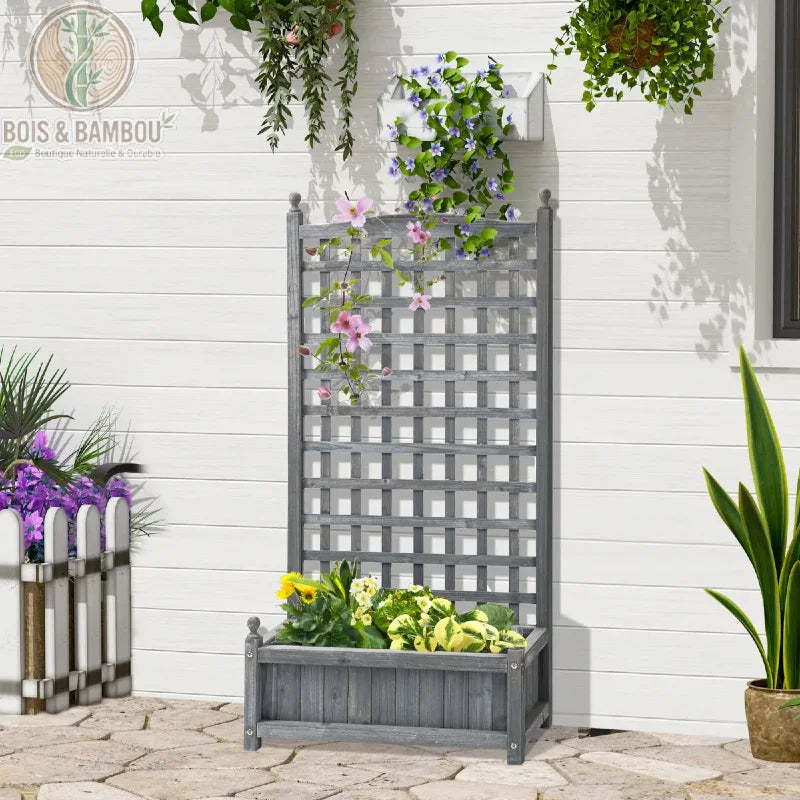 Jardinière en bois avec treillis gris clair. Un bac à fleurs gris avec un grand panneau de treillis décoratif, orné de fleurs grimpantes roses, posé sur une terrasse en pierre.