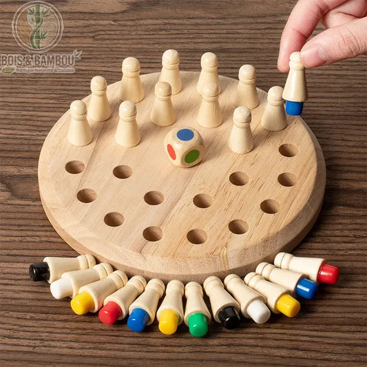 Jeu de mémorisation chromatique en bois. Plateau circulaire avec des pions à base colorée et un dé multicolore. Une main soulève un pion pour révéler sa couleur bleue cachée.