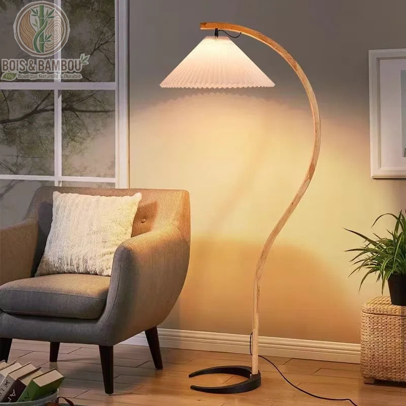 Lampadaire Arc en bois massif , un luminaire élégant avec un pied en bois courbé en arc et un abat-jour plissé blanc, créant un éclairage ciblé et chaleureux au-dessus d'un fauteuil de lecture.