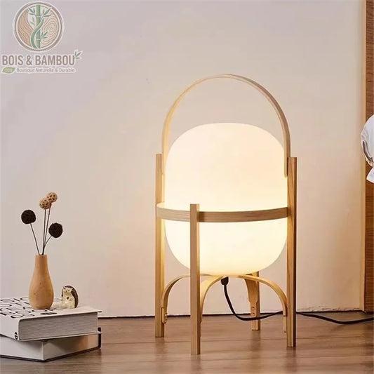 Lampadaire en bois et verre , une lanterne de sol au design moderne avec un diffuseur en verre opalin blanc enchâssé dans une structure légère en bois clair munie d'une anse arrondie.