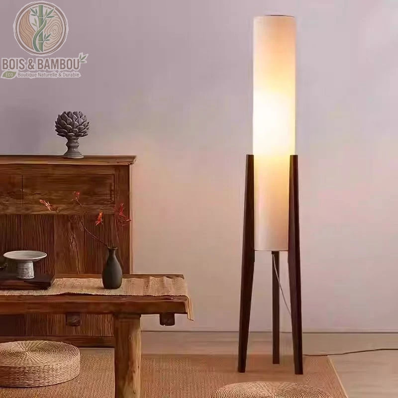 Lampadaire en bois massif , un luminaire sur pied élégant composé d'un long diffuseur cylindrique blanc soutenu par un trépied en bois sombre, parfait pour une ambiance tamisée dans un intérieur minimaliste.
