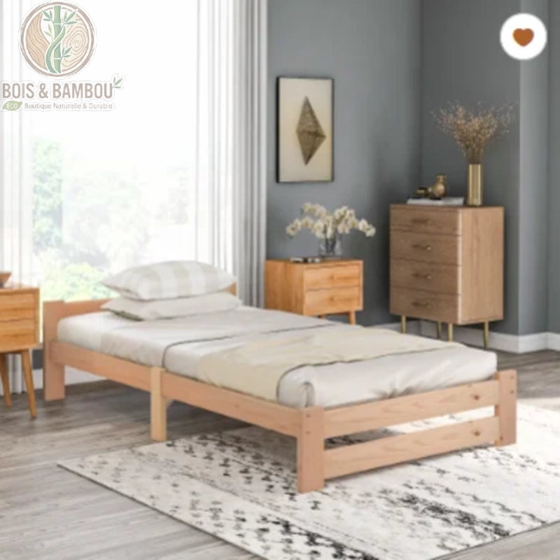 Lit Futon en Bois Massif 90 cm. Un cadre de lit simple et bas en bois clair, sans tête de lit, installé sur un tapis à motifs dans une chambre avec du mobilier assorti.