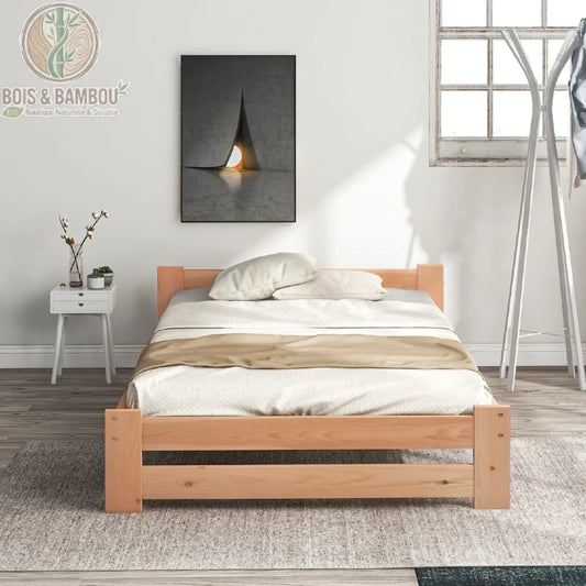 Lit Futon en Bois Massif. Un cadre de lit bas en bois clair au design minimaliste, doté d'une petite tête de lit, placé sur un tapis gris dans une chambre lumineuse et moderne.