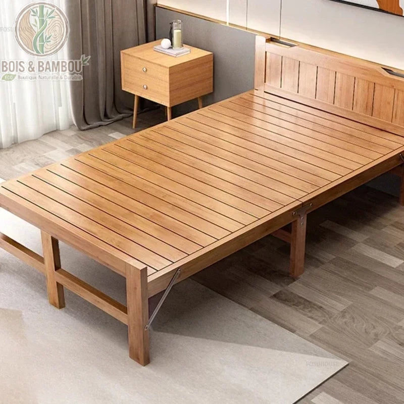 Lit Pliant en Bambou Massif 120x197. Lit d'appoint une place large en bambou massif verni, doté d'un sommier à lattes et d'une tête de lit élégante, installé à côté d'un petit chevet scandinave.