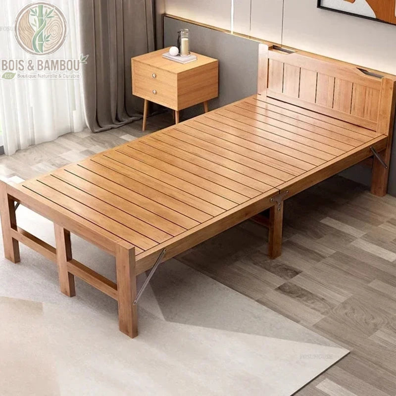 Lit Pliant en Bambou Massif 80x197. Lit simple pliant en bambou massif verni avec sommier à lattes, disposé dans une chambre moderne sur un tapis clair à côté d'une table de chevet en bois assortie.