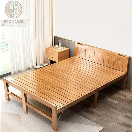 Lit Pliant en Bambou Massif. Un lit double pliable en lattes de bambou naturel avec tête de lit intégrée, installé dans une chambre lumineuse à côté d'une table de nuit assortie.