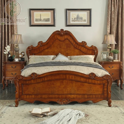 Lit en Acajou Massif Traditionnel. Un lit somptueux en bois foncé sculpté avec une tête de lit imposante, encadré par deux tables de chevet assorties dans une chambre classique.