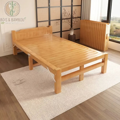 Lit en Bambou Massif Classique 100x190x35. Lit une place large en bambou massif au fini naturel, présenté sur un tapis dans une chambre zen, avec un modèle identique replié contre le mur pour le gain de place.