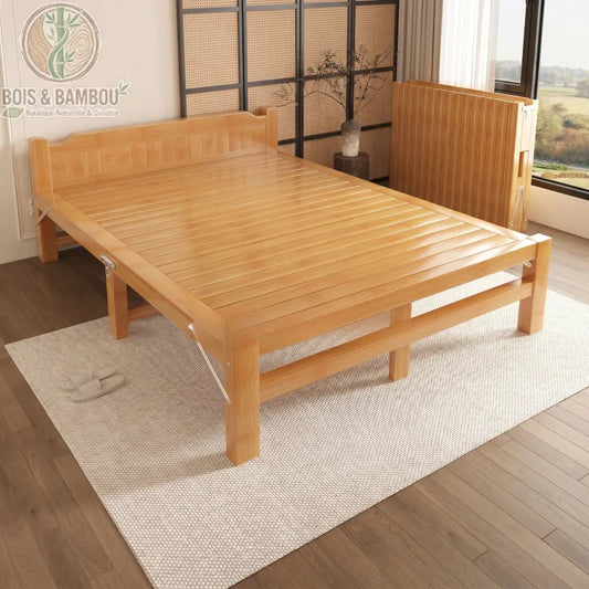 Lit en Bambou Massif Classique. Un cadre de lit pliable en bambou clair aux lignes épurées, présenté ouvert sur un tapis beige et replié contre le mur dans une chambre moderne.