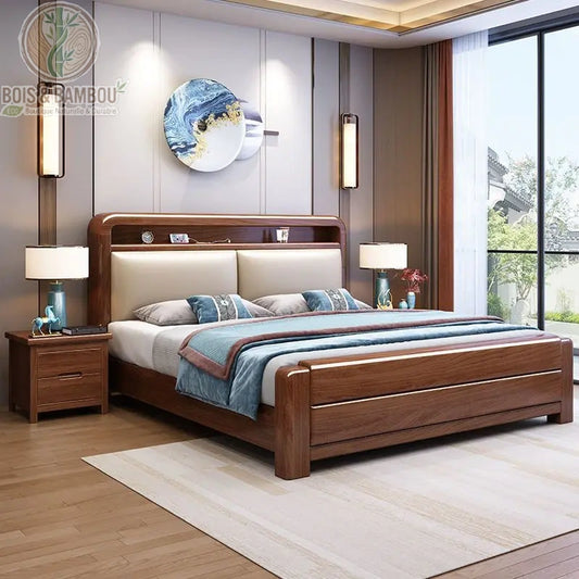 Lit en Noyer de Soie Dorée. Un lit luxueux en bois massif foncé avec une tête de lit rembourrée beige intégrant une niche de rangement, entouré de deux tables de chevet assorties.