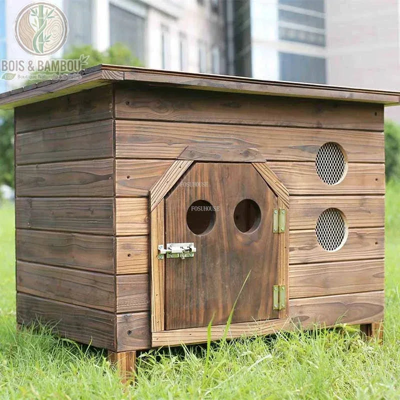 Maisonnette Nordique en Bois. Une niche extérieure en bois brun foncé avec une porte à loquet munie de deux hublots et des ouvertures aérées sur le côté, posée dans l'herbe.