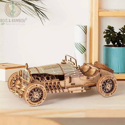 Maquette de voiture en bois. Une réplique miniature détaillée d'une voiture ancienne de sport, assemblée en bois découpé au laser, posée sur un meuble clair avec des plantes.