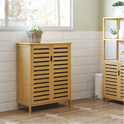 Meuble Bas de salle de bain en bambou. Un placard bas en bois clair avec deux portes persiennes, surmonté d'un panier de fleurs, placé contre un mur carrelé blanc dans une salle de bain.