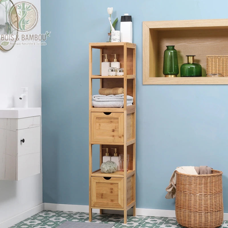 Meuble de salle de bain en bambou. Une étagère colonne étroite en bois clair avec deux tiroirs et trois niches de rangement, installée dans une salle de bain aux murs bleus.