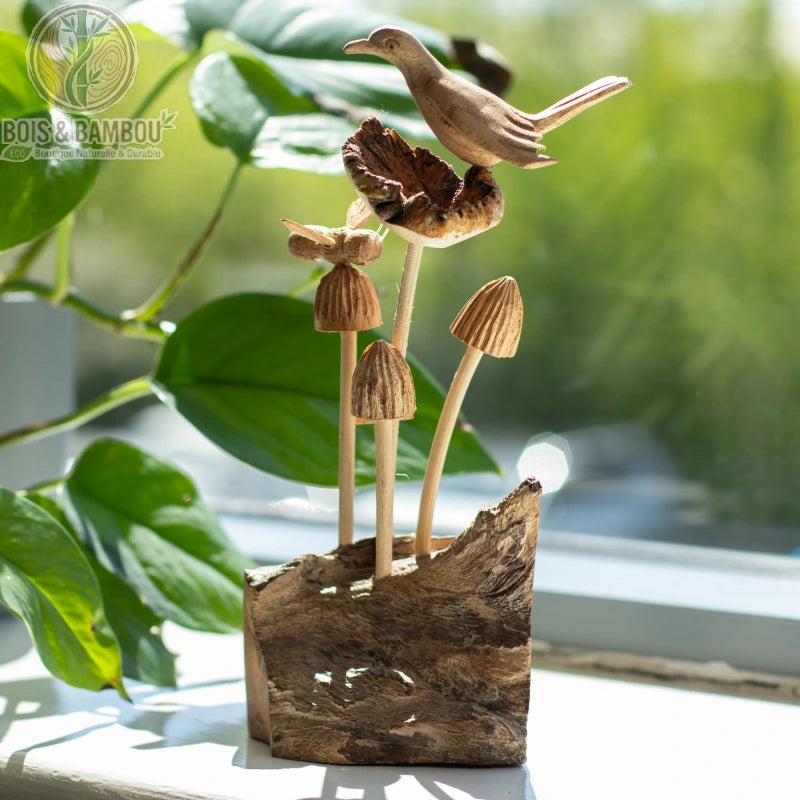 Sculpture oiseau bois perché sur des champignons devant un feuillage
