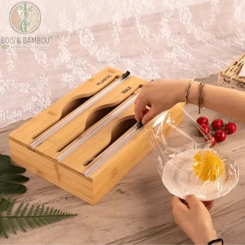 Organisateur de cuisine en bambou 2-en-1. Un distributeur en bois avec curseurs de coupe pour film plastique et papier ciré, utilisé pour recouvrir une assiette de fruit.