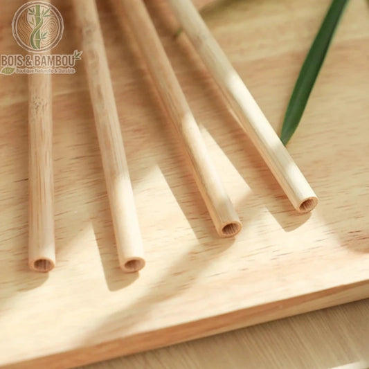 Pailles en bambou réutilisables. Quatre pailles en bambou naturel disposées parallèlement sur une planche en bois clair sous une lumière naturelle. Alternative écologique zéro déchet.