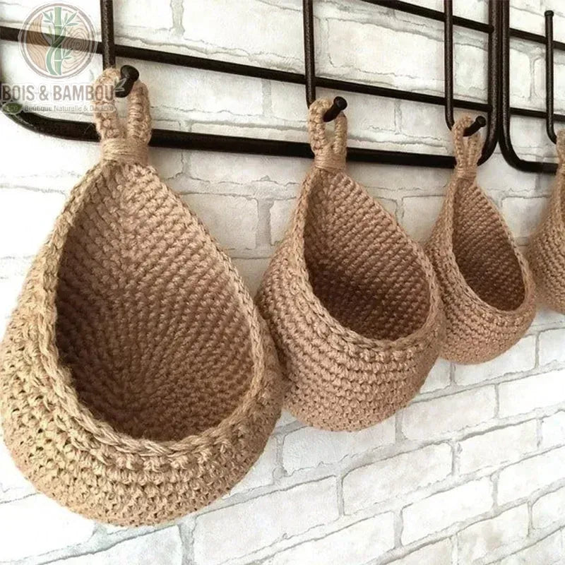 Panier Mural en Osier. Trois paniers suspendus en jute tressée de tailles graduées, accrochés à un support métallique noir devant un mur en briques blanches. Rangement mural bohème.