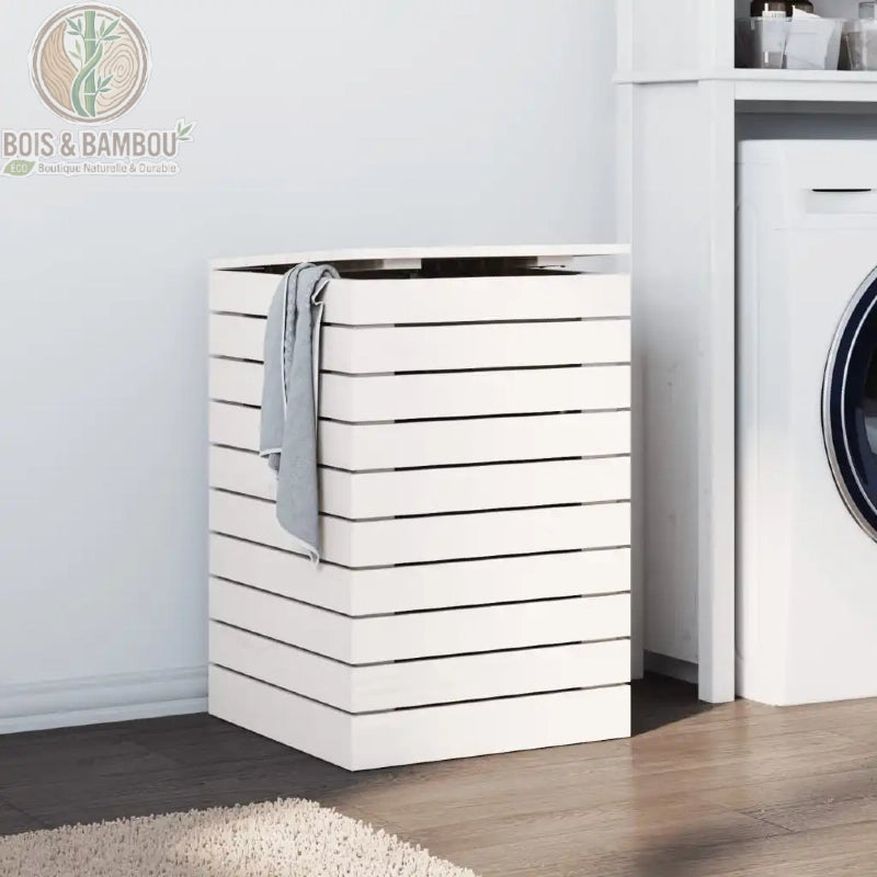 Panier a Linge en Pin Massif blanc 44 44 66 cm. Coffre à linge contemporain en bois de pin blanc avec structure à lattes horizontales et couvercle, placé dans une buanderie claire près d'une machine.