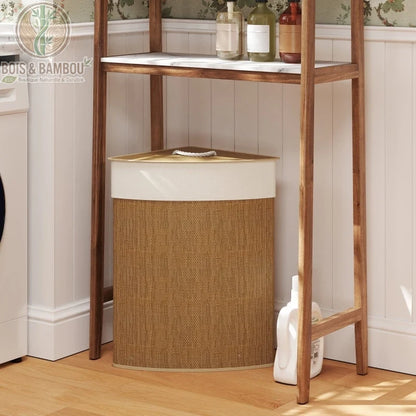 Panier à linge d'angle en bambou. Structure triangulaire avec couvercle blanc et corps tressé. Placé sous une étagère en bois avec des bouteilles de savon dans une salle de bain zen.
