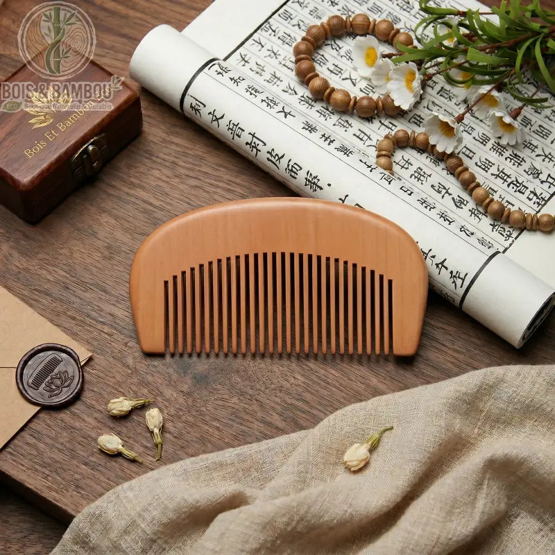 Peigne de Poche en Bois Naturel demi-lune, dents larges. Sur table en bois avec rouleau calligraphie, perles, fleurs blanches, tissus, cachet de cire. Accessoire beauté bio.