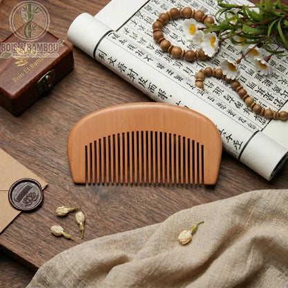 Peigne de Poche en Bois Naturel demi-lune, dents larges. Sur table en bois avec rouleau calligraphie, perles, fleurs blanches, tissus, cachet de cire. Accessoire beauté bio.
